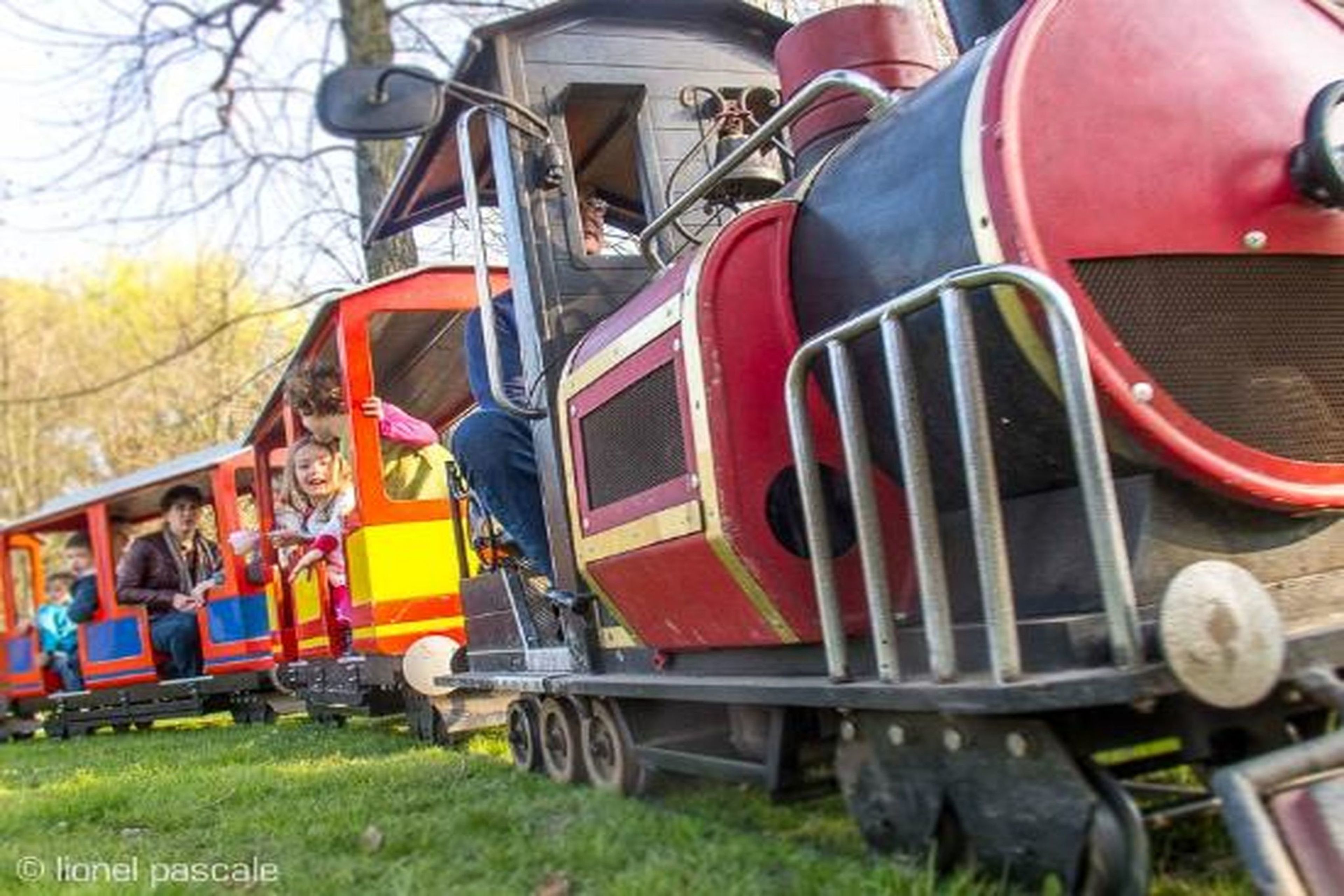 A small train with passengers, moving on tracks in a park.