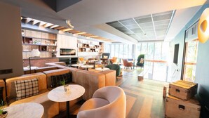Un área de estar moderna con asientos, mesas y una cocina al fondo.