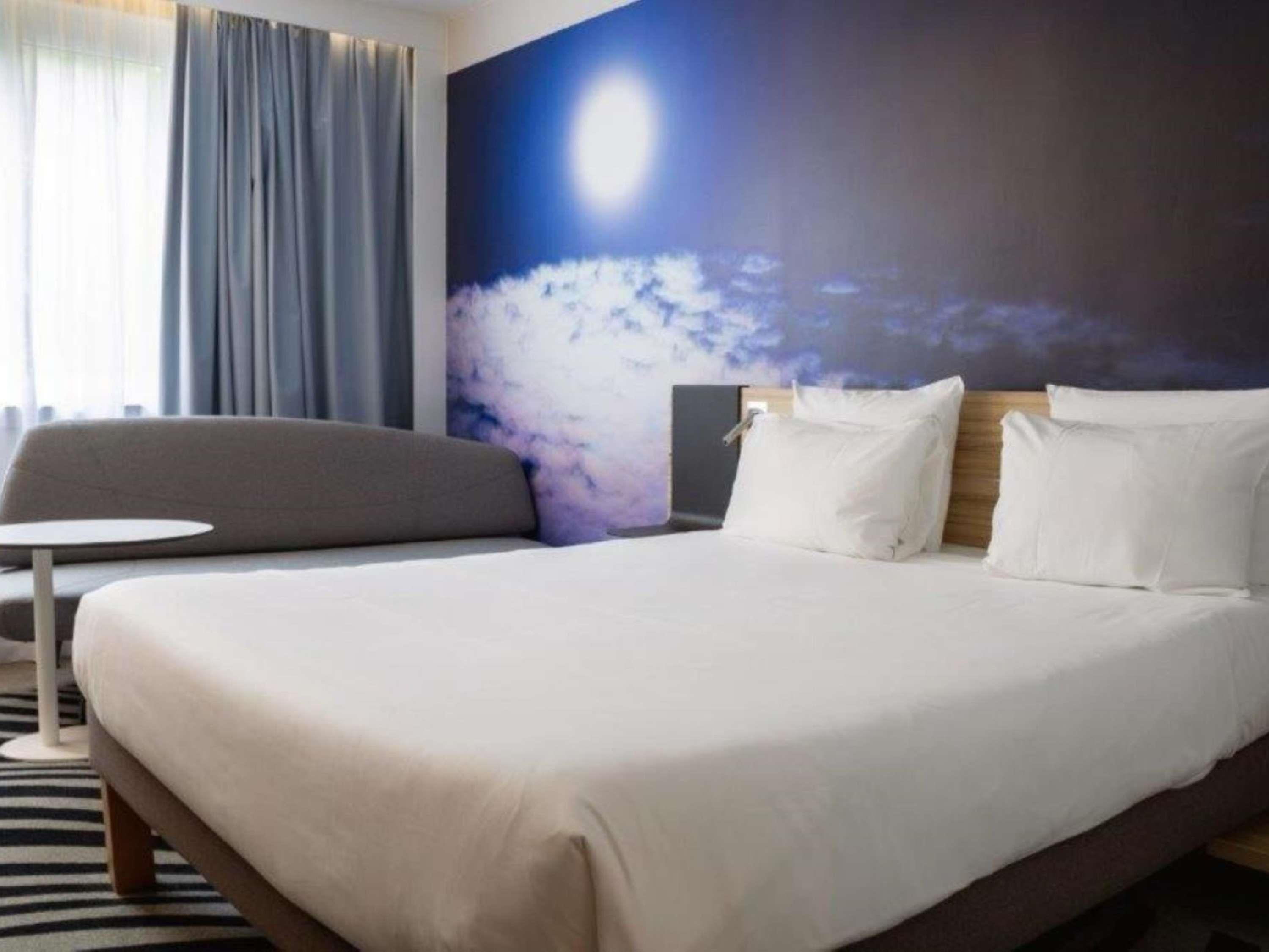 Une chambre d’hôtel avec un lit, une petite table ronde, un canapé et une grande fresque murale.