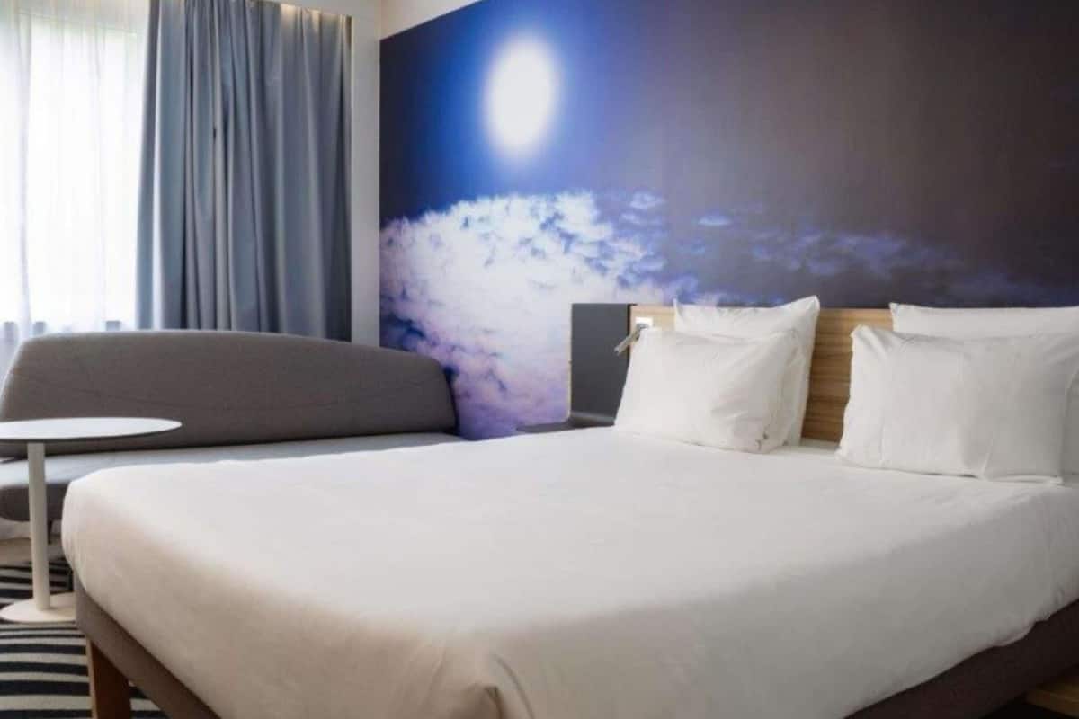 A hotel room with a bed, a small round table, a sofa, and a large wall mural.