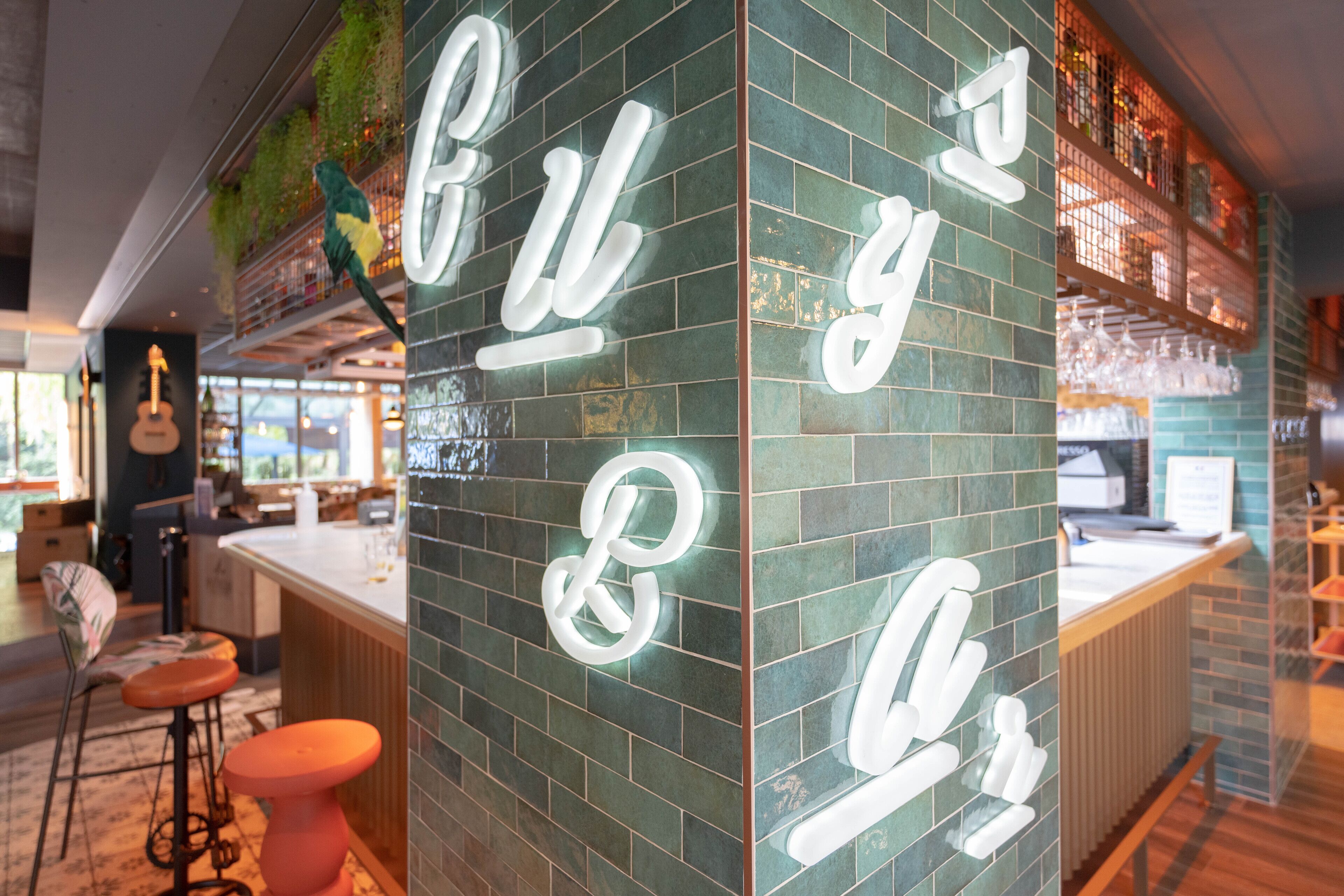 Un espace bar avec un mur recouvert de carreaux verts et un panneau néon indiquant « Bar & Grill ».
