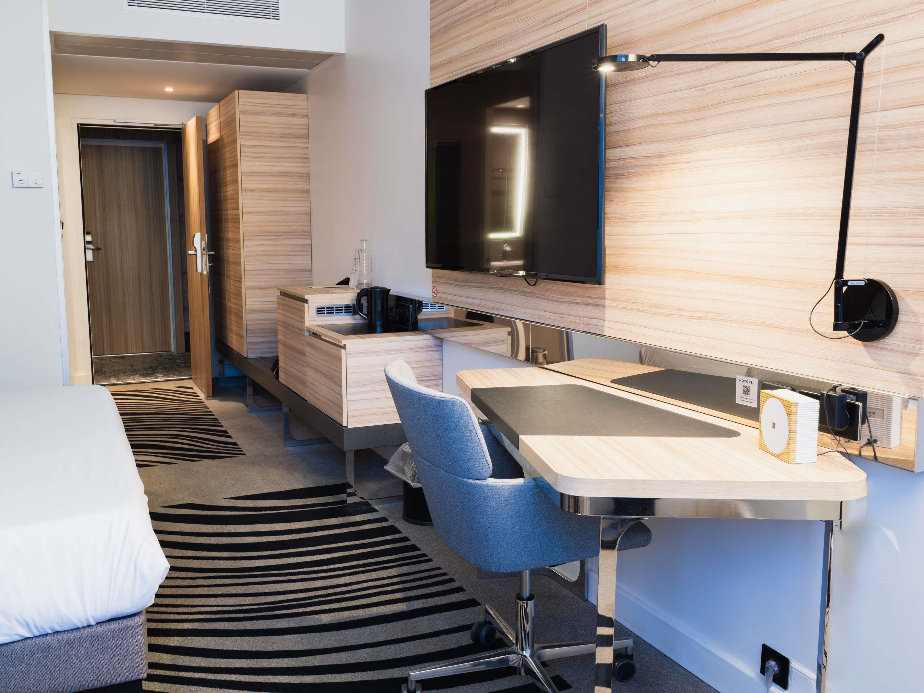 Una habitación de hotel moderna con una cama, un escritorio con una silla, un televisor de pantalla plana, una lámpara de escritorio y un mini bar.