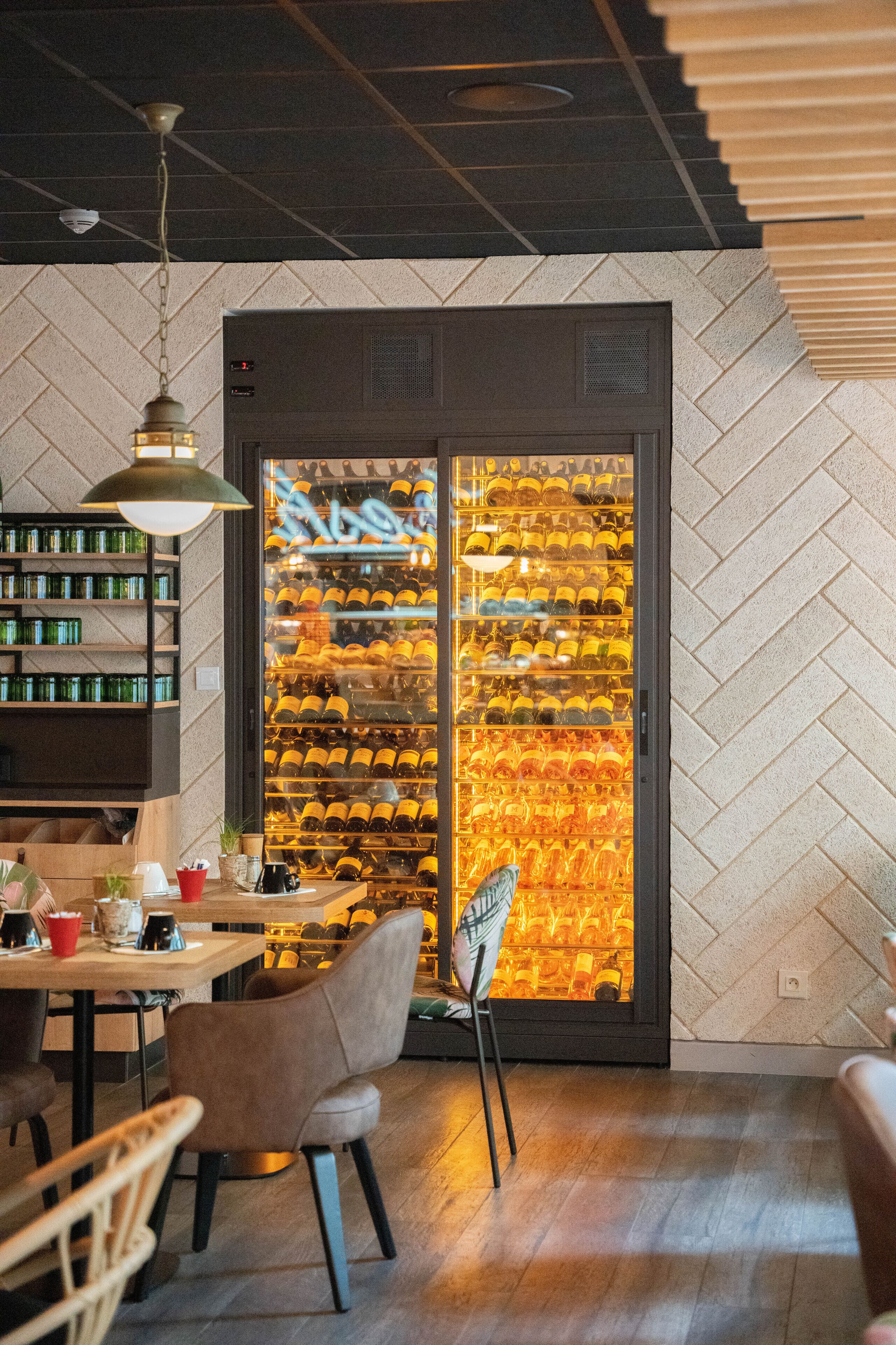 Et restaurantinteriør med et vinskab, træhylder og en væg med et fiskebensmønster.