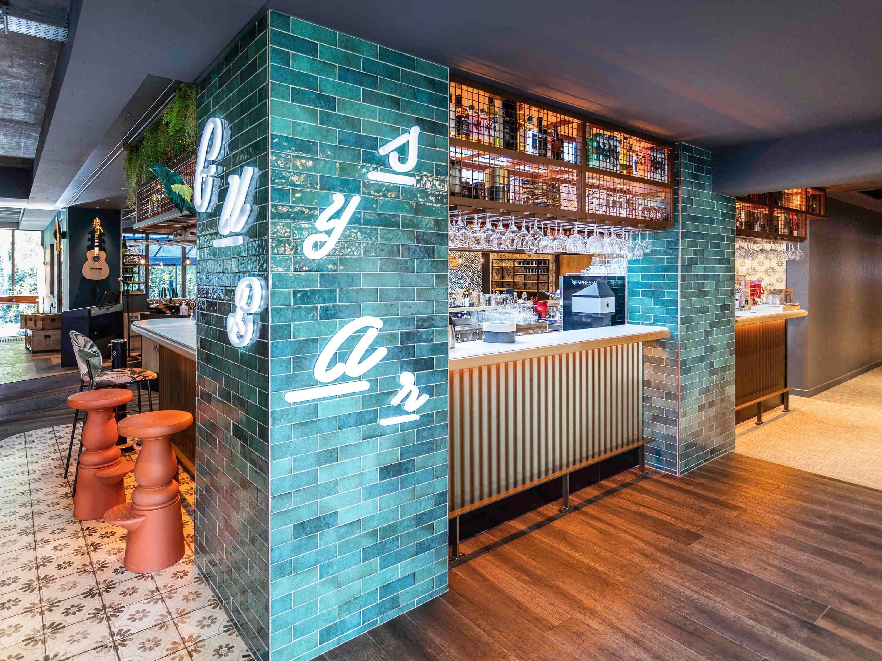 A bar area with a green-tiled wall, a counter with a coffee machine, and stools.