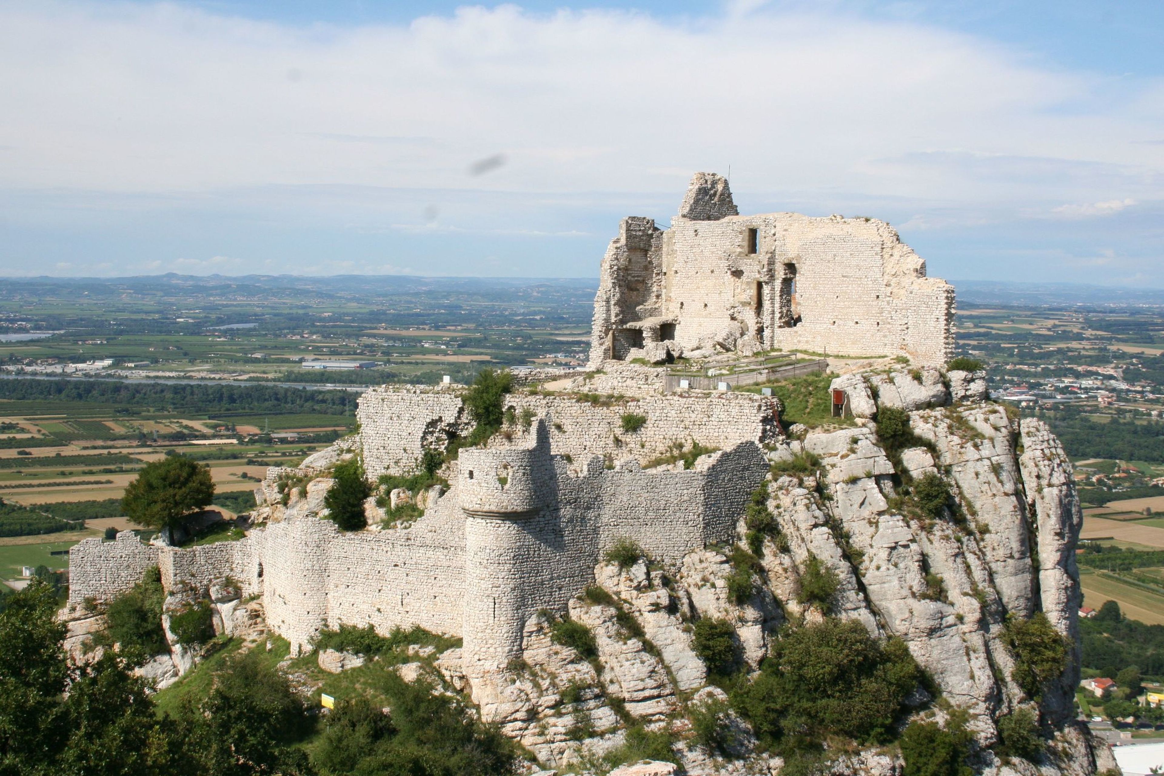 Un castillo de piedra histórico en una colina rocosa, con una vista panorámica del campo.