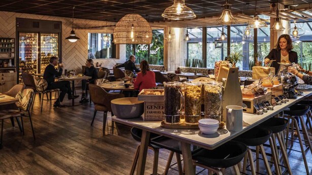 Restaurante con techo a cuadrícula, suelo de madera y lámparas colgantes. Las mesas están preparadas con distintos platos y condimentos.