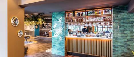 Una zona de bar con una barra, estantes llenos de botellas y una persona trabajando detrás.