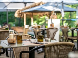 An outdoor dining area with wicker furniture, glass candle holders, and a thatched umbrella.