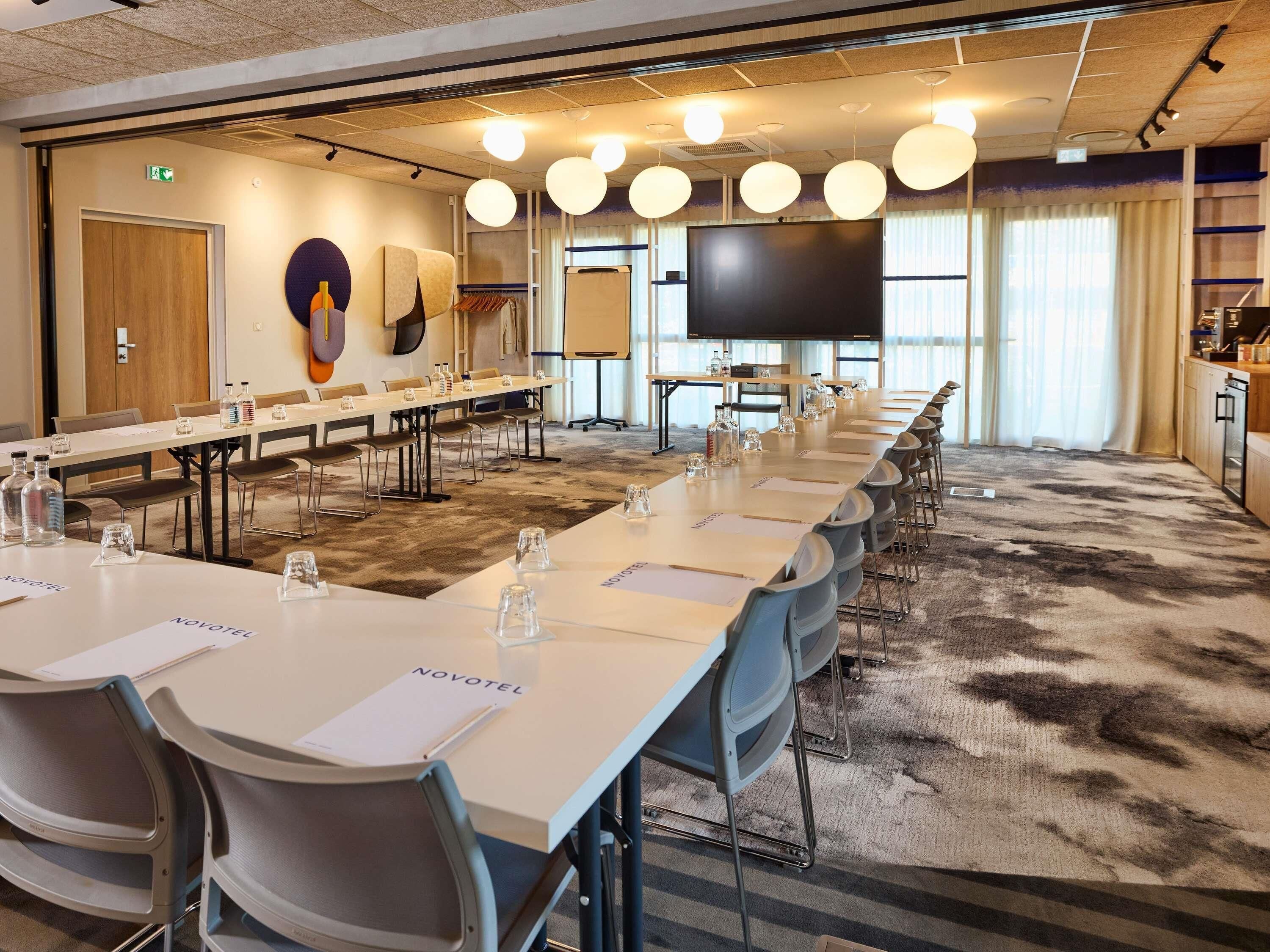 A conference room with long tables, chairs, a TV screen, and a carpeted floor.