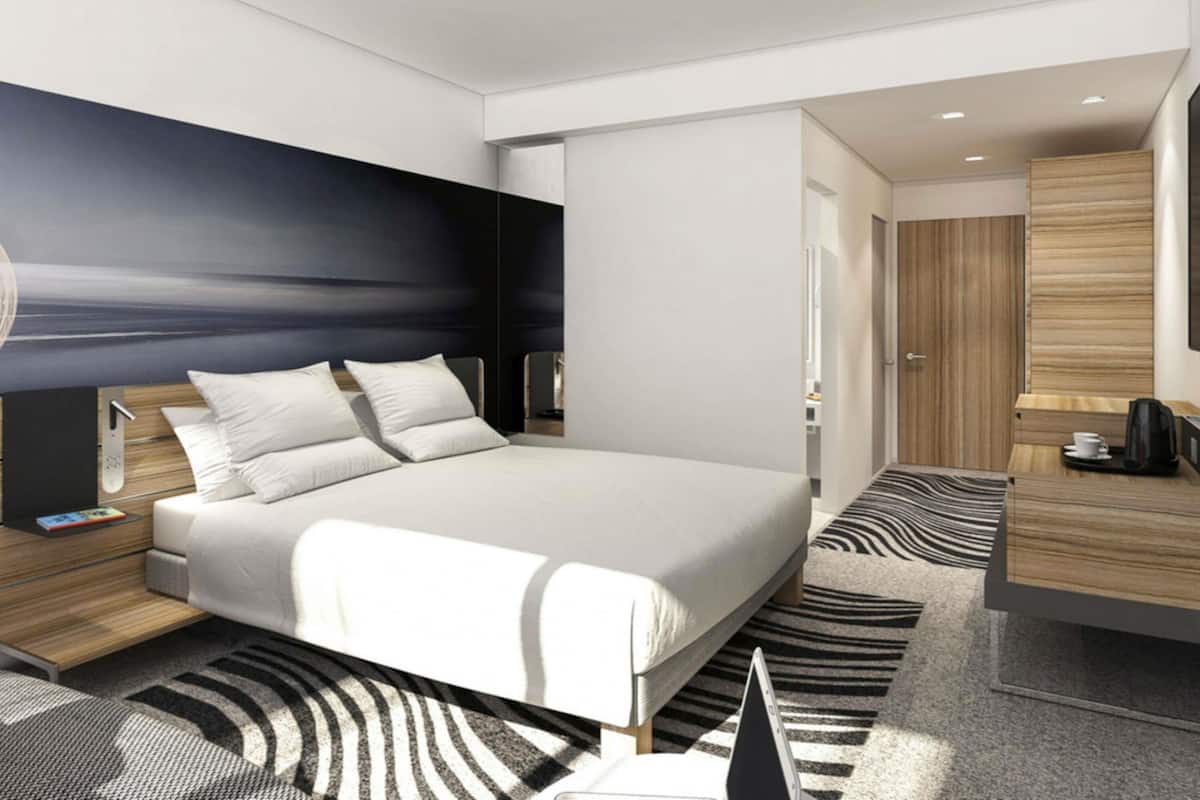 A modern hotel room with a large bed, bedside tables, a desk, and a wardrobe.