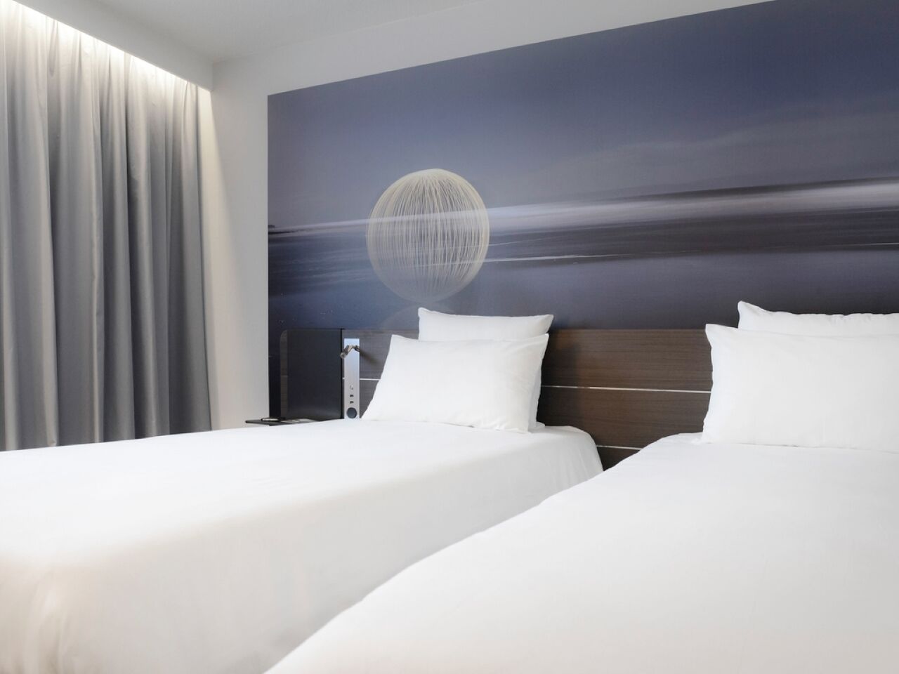 A hotel room with two beds, a large window with curtains, and a wall mural.