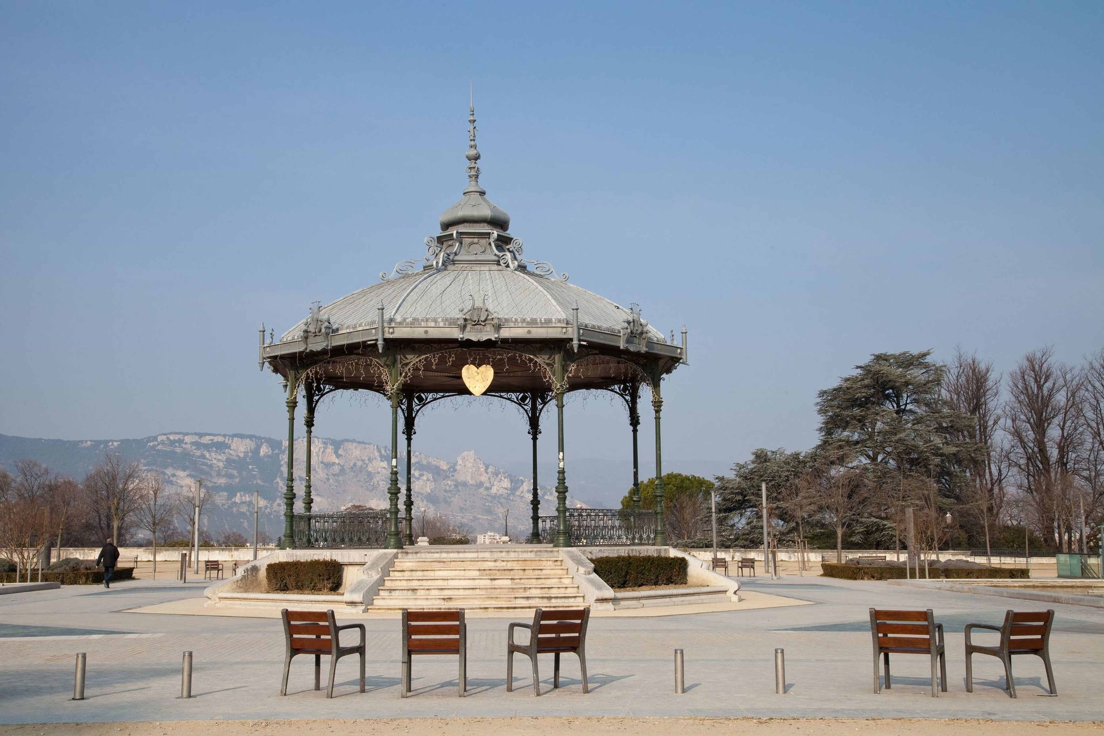 A gazebo with a dome roof and a heart-shaped window, surrounded by benches and a clear sky.