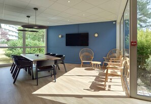 A conference room with a large table, chairs, a flat-screen TV, and a view of greenery outside. - B&B HOTEL Cergy Port (Cergy)