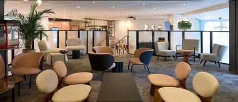 Un espace de détente moderne offrant de nombreuses options d’assises, notamment des canapés et des fauteuils, ainsi qu’une machine à café et un téléviseur.