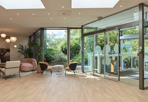 A modern interior with a glass wall, wooden flooring, and a seating area with two chairs and a table. - B&B HOTEL Cergy Port (Cergy)