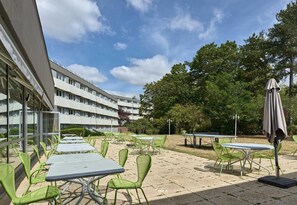 Un patio al aire libre con mesas y sillas, un edificio al fondo y árboles.