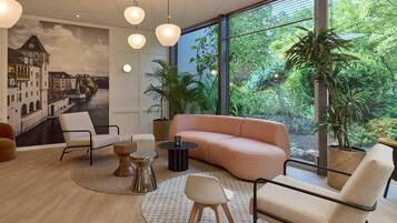 Un intérieur moderne avec une grande fenêtre, un canapé, des fauteuils, une table ronde et une fresque représentant un paysage urbain.