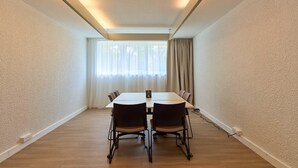 A conference room with a long table, four chairs, a window with curtains, and a ceiling light.