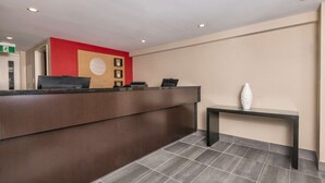 Un mostrador de recepción con una pared de acento roja, un banco negro y un jarrón blanco.