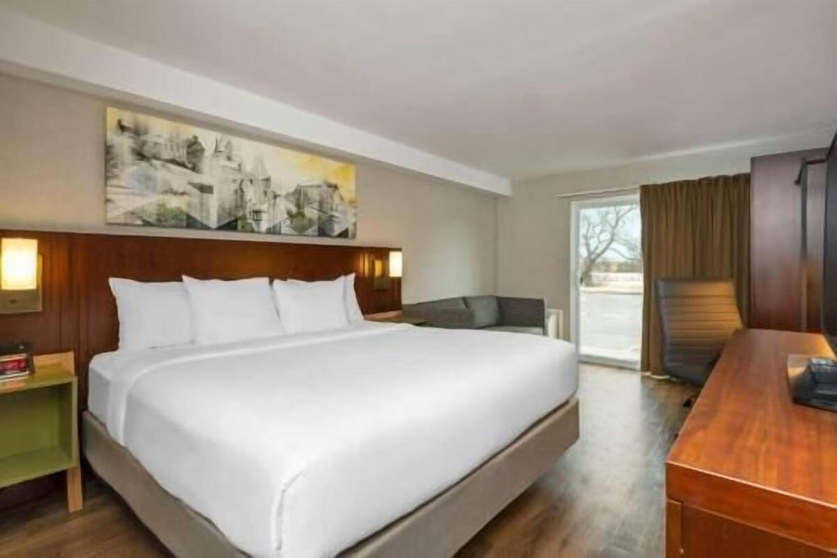A hotel room with a large bed, a desk, a chair, a painting on the wall, and a window.