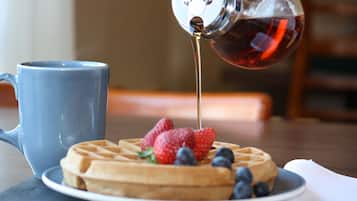 A waffle topped with strawberries and blueberries, a blue mug, and syrup being poured onto the waffle.