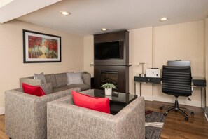 A modern living room with a sofa set, a flat-screen TV, a fireplace, and a desk with a chair.