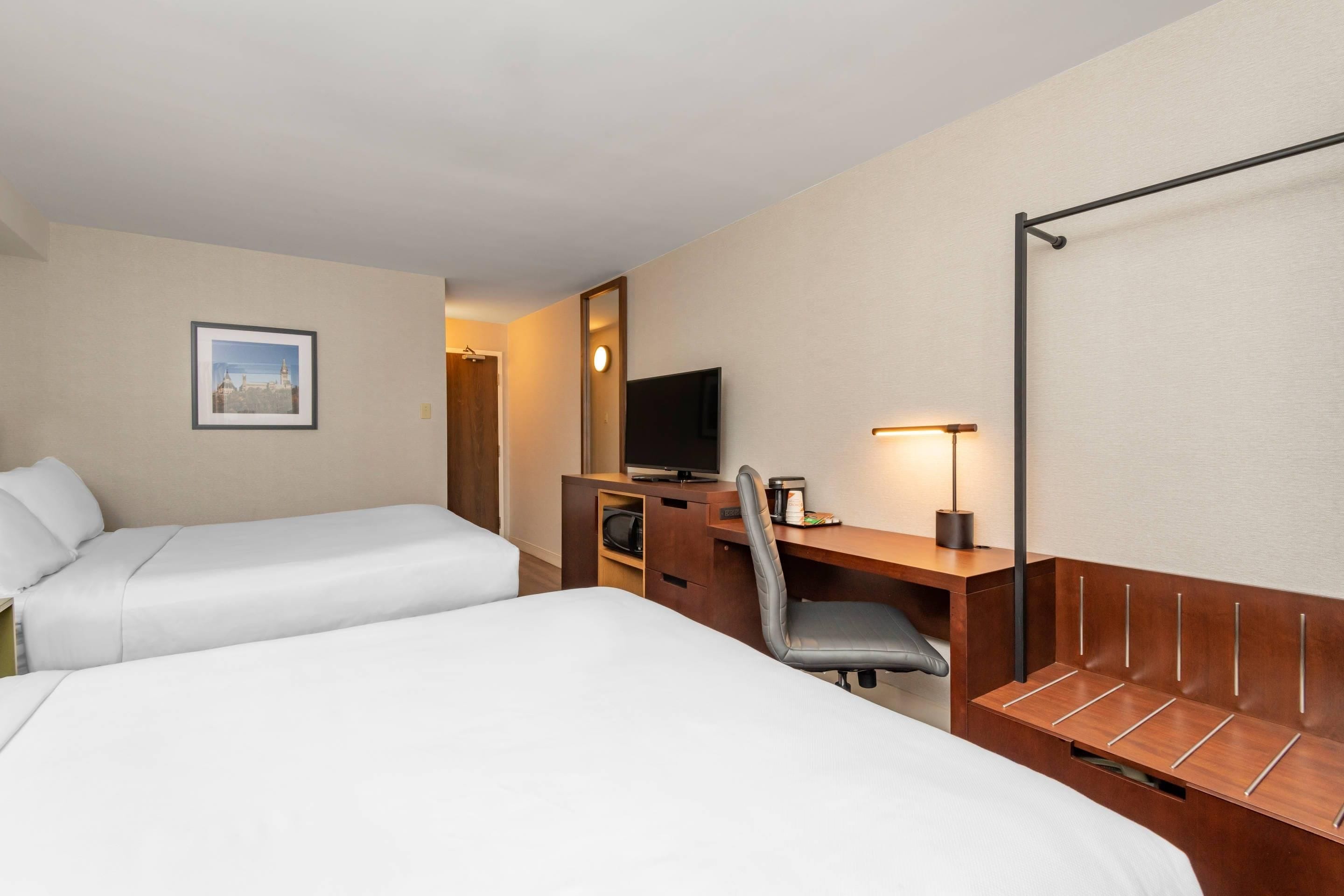 Habitación de hotel con dos camas, un escritorio con silla, televisión y un cuadro en la pared.