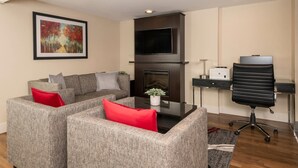 Ein modernes Wohnzimmer mit einem Ecksofa, einem Kamin, einem Flachbildfernseher und einem Schreibtisch mit Stuhl.