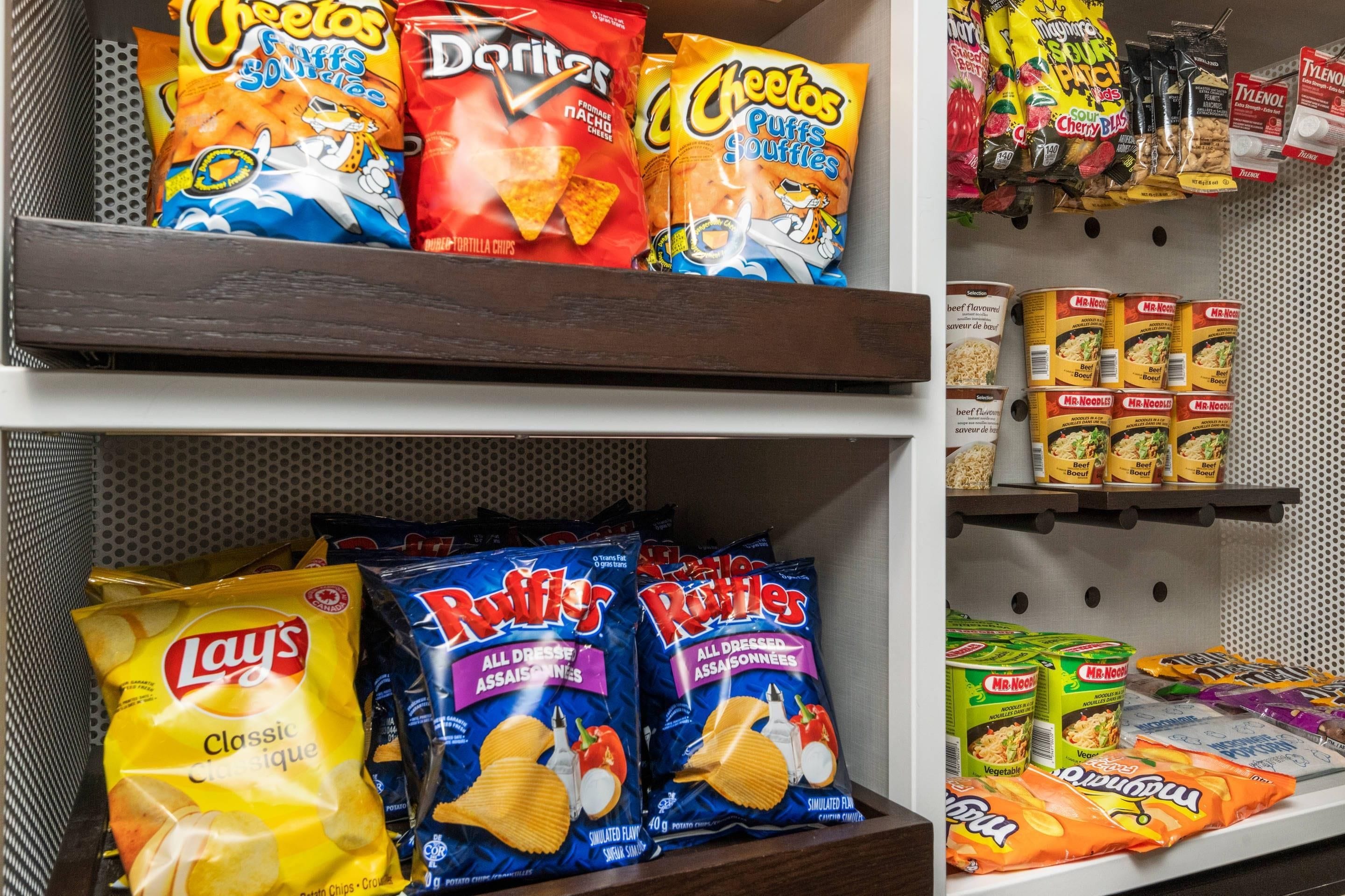Des étagères remplies de différentes marques de collations, notamment Cheetos, Doritos, Lay's, Ruffles et Mr. Noodle.