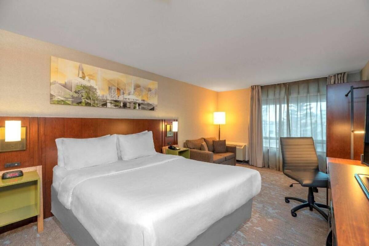 A hotel room with a large bed, a desk, a chair, a sofa, and a painting on the wall.
