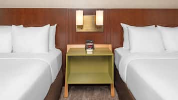 A hotel room with two beds, a nightstand with a clock, and a wall-mounted light fixture.