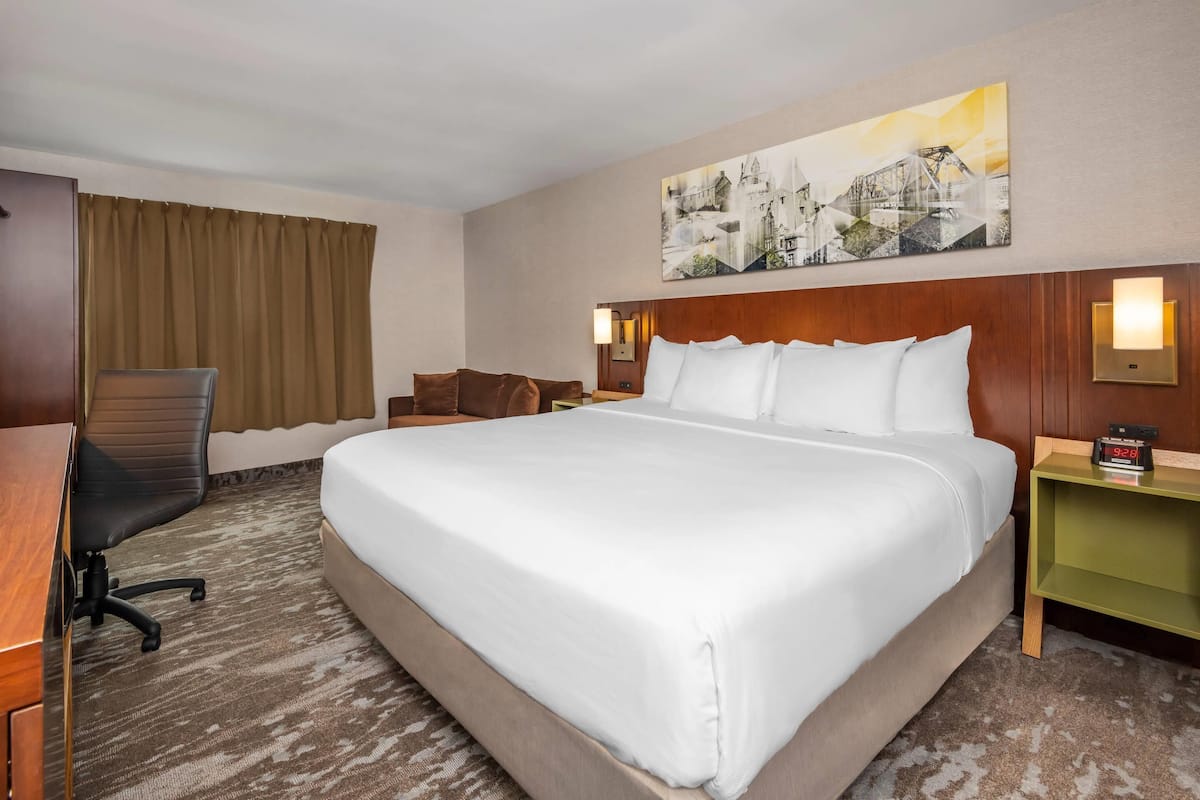 A hotel room with a large bed, a desk, a chair, and a painting on the wall.