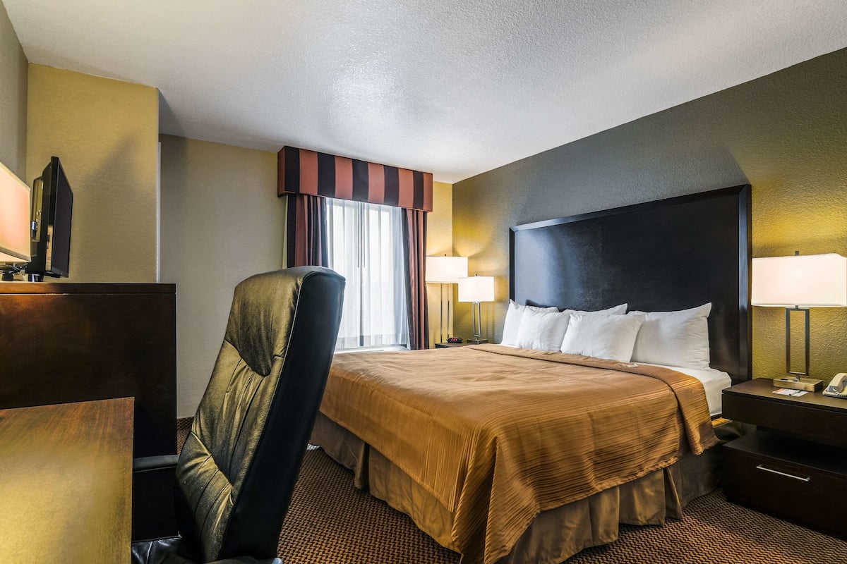 A hotel room with a large bed, a chair, a desk, and a lamp.