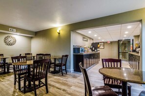Un restaurante con mesas y sillas de madera, una zona de cocina y un suelo de baldosas.