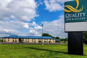 Un Quality Inn & Suites con un edificio de techo azul, estacionamiento y un área verde.
