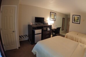 Una habitación de hotel con una cama, un escritorio con televisor, una silla y un refrigerador pequeño.