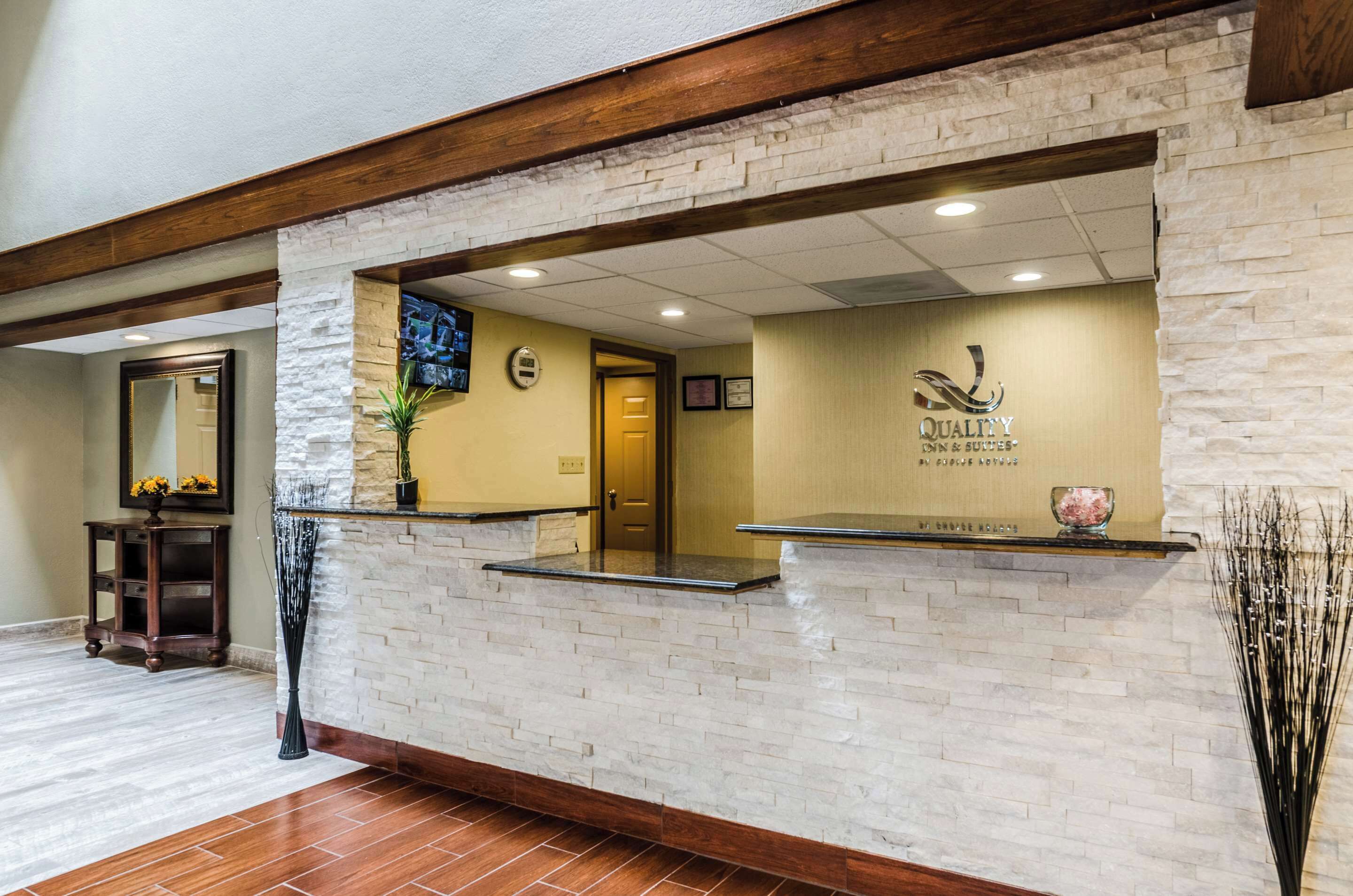 Una zona de recepción con pared de piedra, vigas de madera, mostrador de recepción, un espejo y una puerta.