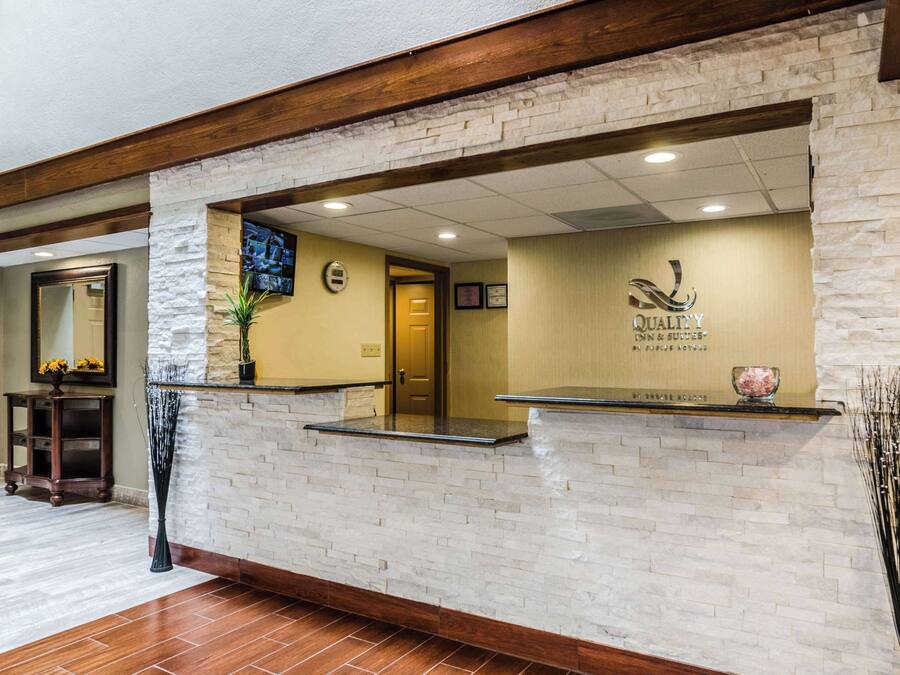 Una zona de recepción con pared de piedra, vigas de madera, mostrador de recepción, un espejo y una puerta.