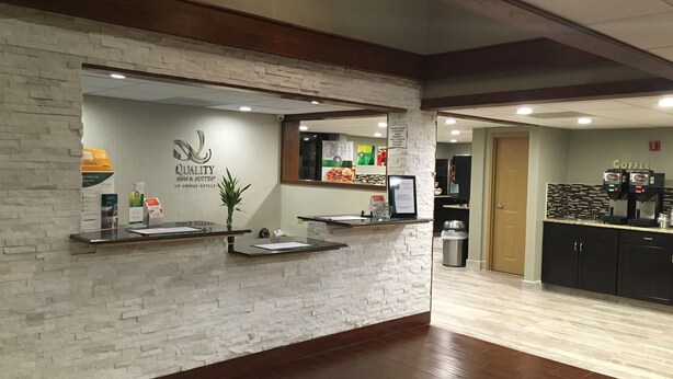 A reception area with a stone wall, a reception desk, a coffee machine, and a trash can. - Quality Inn & Suites Winfield (Winfield)