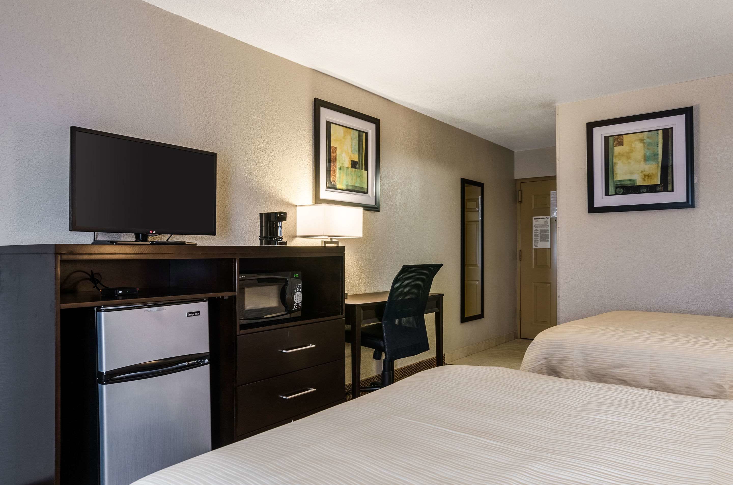 A hotel room with a bed, a desk with a chair, a television, a refrigerator, and a microwave. There are two framed pictures on the wall.