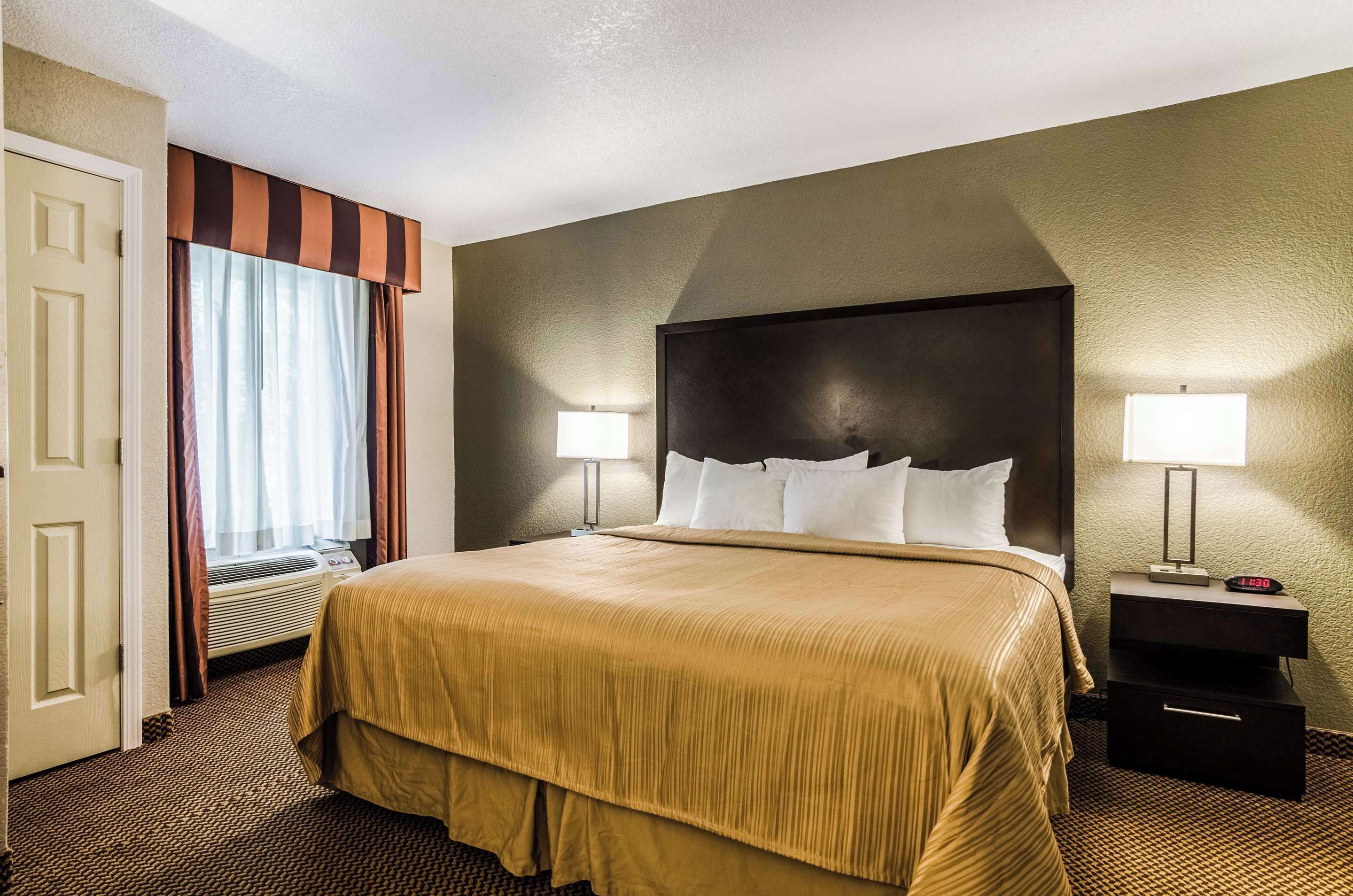 Habitación de hotel con una cama grande, dos lámparas de noche, una mesita de noche y un ventanal con cortinas.