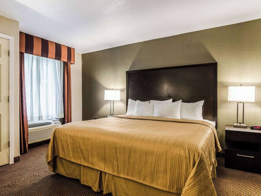 Habitación de hotel con una cama grande, dos lámparas de noche, una mesita de noche y un ventanal con cortinas.