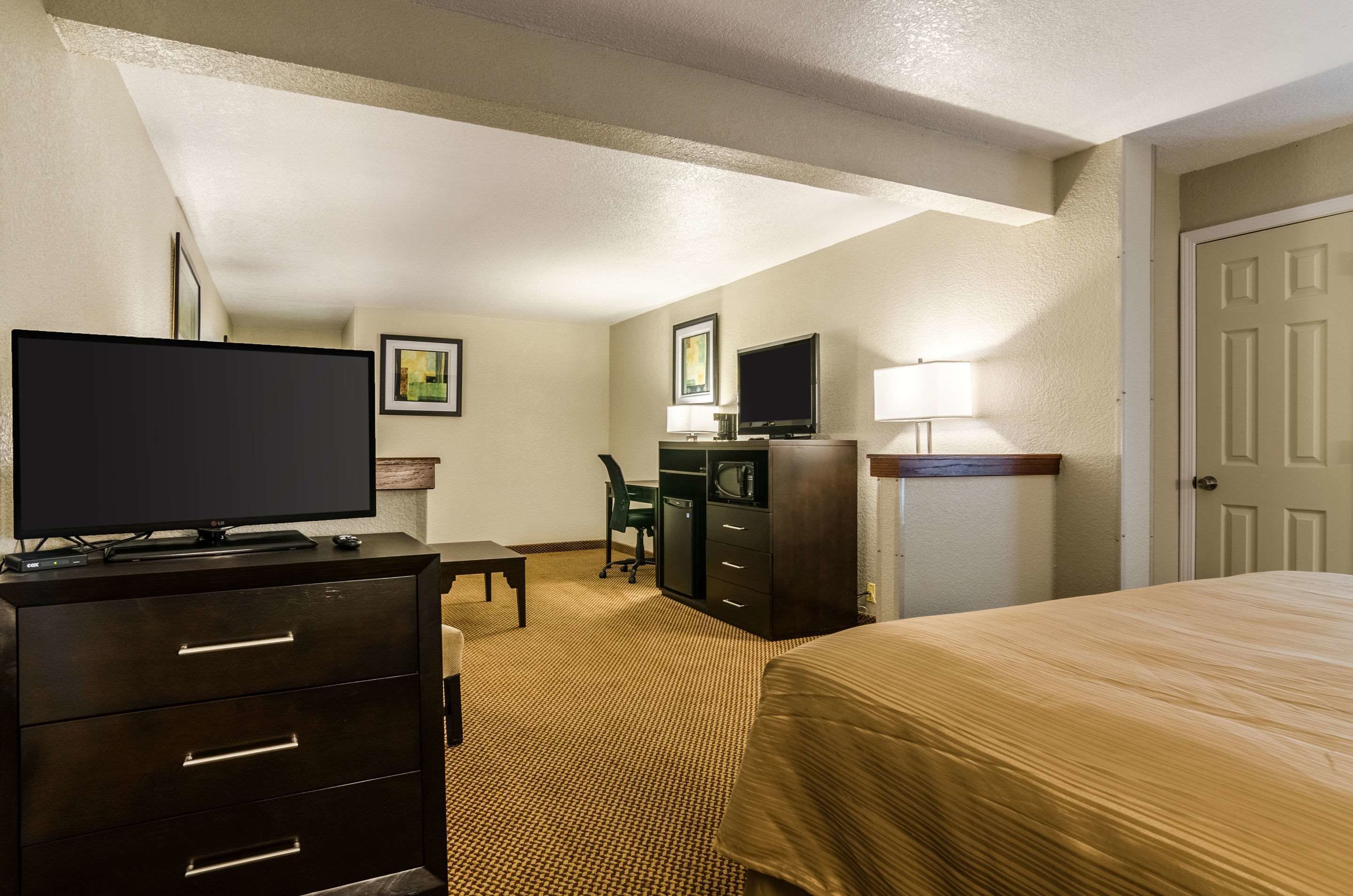 A hotel room with a bed, a TV on a dresser, a desk with a chair, and a lamp.