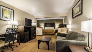 Una habitación de hotel con cama, sofá, escritorio con silla, televisión y una mesita.