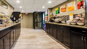 A hotel kitchen with a long counter, various food items, and a coffee machine. - Quality Inn & Suites Winfield (Winfield)