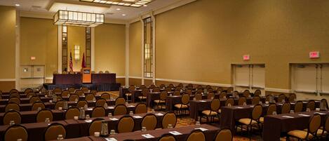 A conference room with rows of tables and chairs, a podium, and exit signs.
