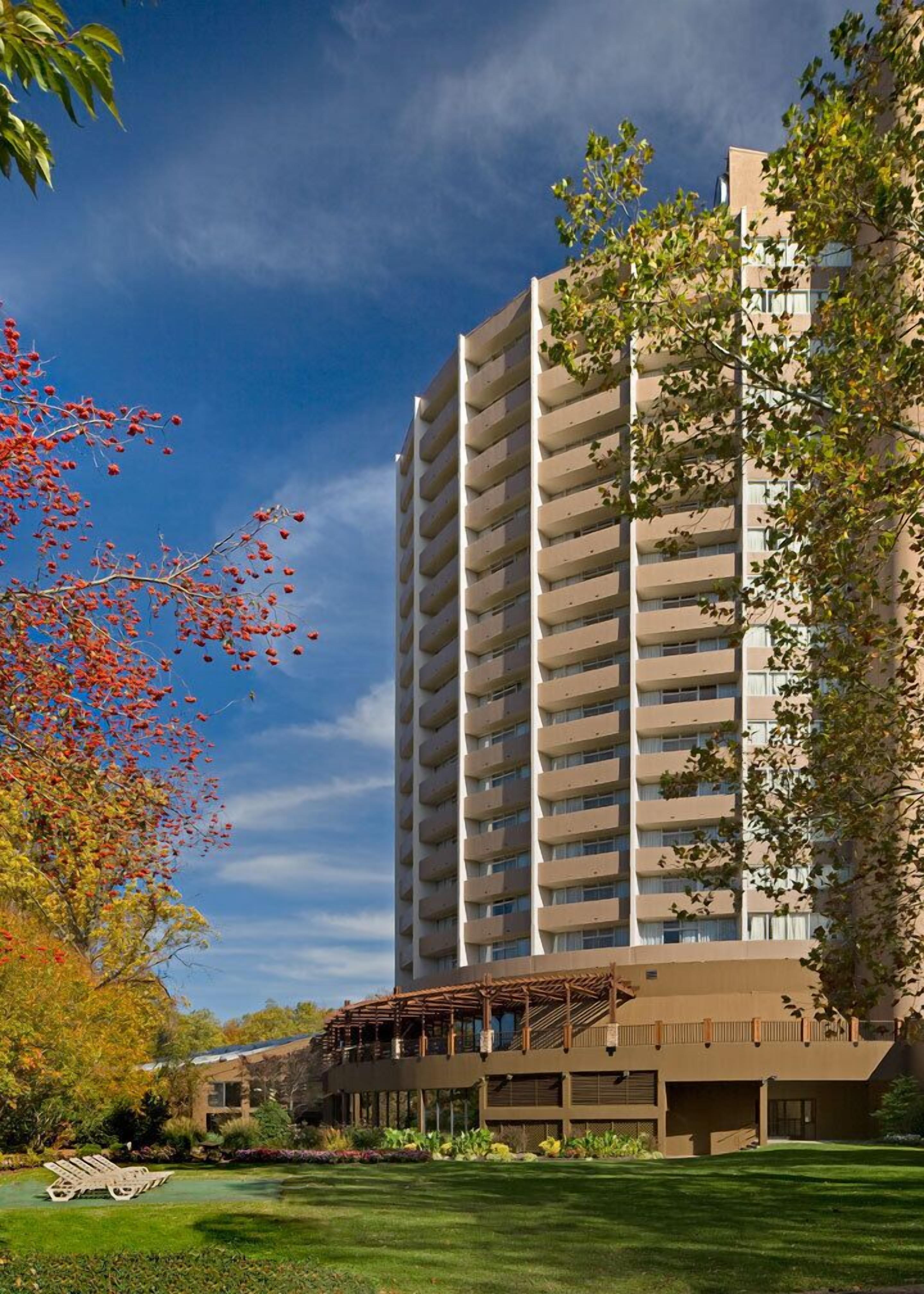 A high-rise building with multiple balconies, surrounded by lush greenery and a well-maintained lawn.