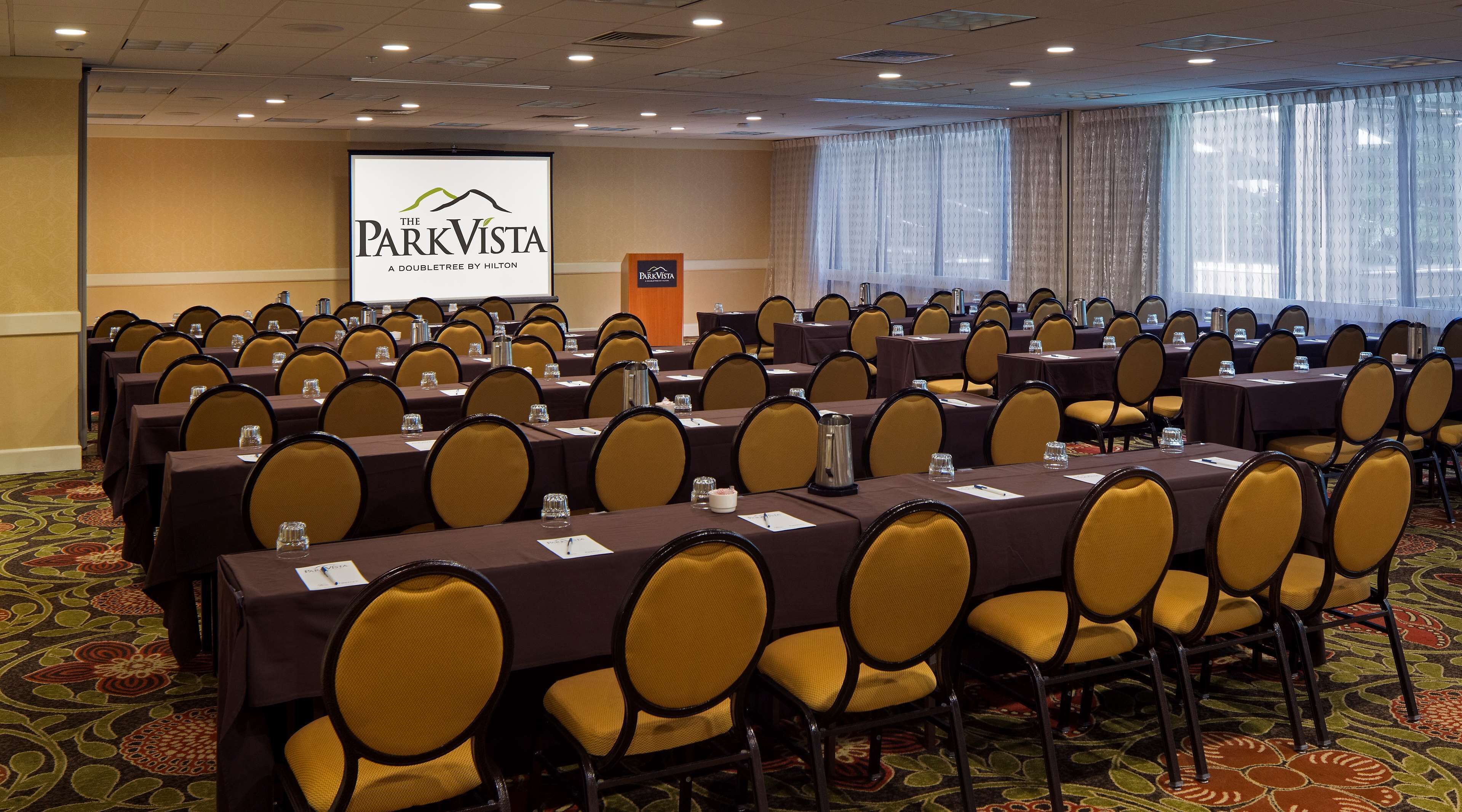 A conference room with rows of tables and chairs, a podium, and a screen displaying 'The ParkVista A Doubletree by Hilton'.