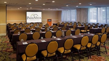 A conference room with rows of tables and chairs, a podium, and a screen displaying 'The ParkVista A Doubletree by Hilton'.