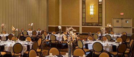 A banquet hall with round tables set for dining, featuring white tablecloths, chairs, and centerpieces.